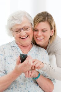 Young smiling granddaughter showing and teaching a mobile phone to her grandmother